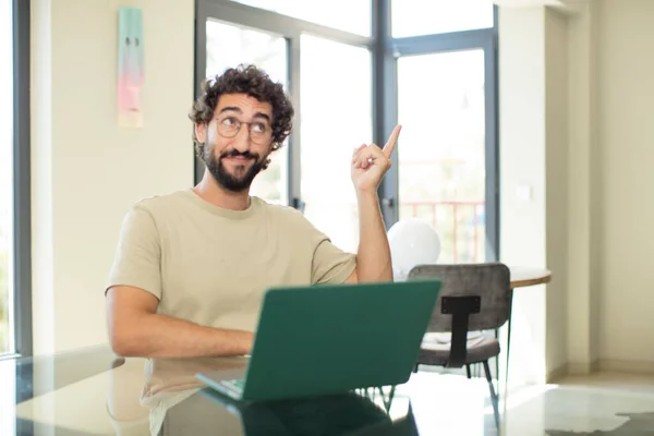 一个留着胡子的年轻人 带着笔记本电脑快乐地微笑着 侧视着 纳闷着 思考着或有个主意 — 图库照片