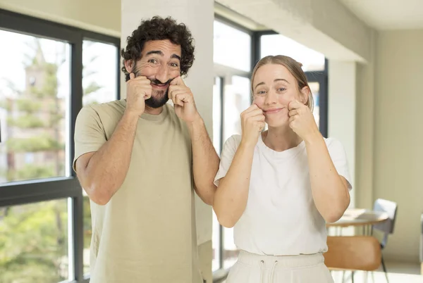 young adult couple smiling and pointing to own fake smile