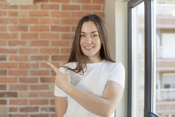 stock image young adult pretty woman smiling cheerfully, feeling happy and pointing to the side and upwards, showing object in copy space