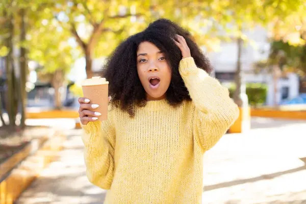 pretty afro black woman feeling extremely shocked and surprised. take away coffee concept