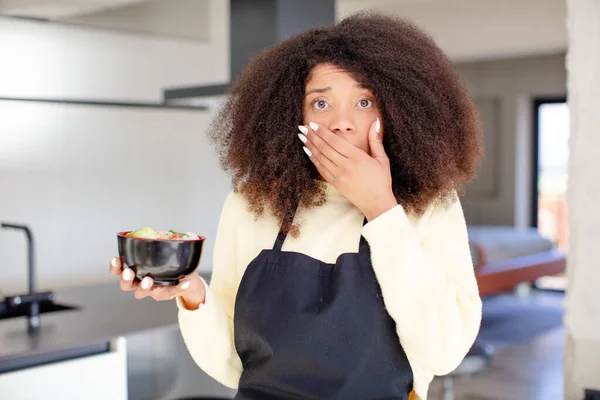pretty afro black woman covering mouth with a hand and shocked or surprised expression. japanese noodles ramen concept
