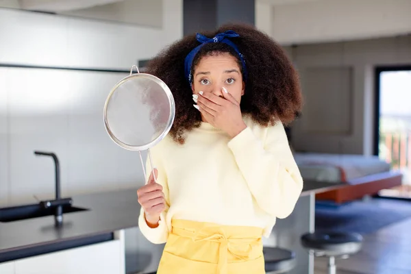 pretty afro black woman covering mouth with a hand and shocked or surprised expression. home chef concept