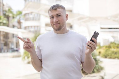 Neşeli bir şekilde gülümsüyor, mutlu hissediyor ve bir tarafı işaret ediyor. akıllı telefon kavramı