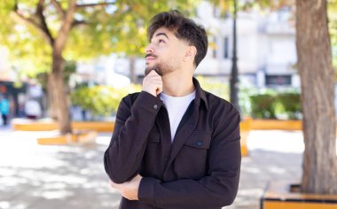 Genç yakışıklı adam mutlu bir şekilde gülümsüyor ve hayal kuruyor ya da şüphe ediyor.