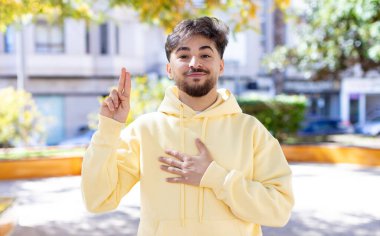 Genç yakışıklı adam mutlu, kendinden emin ve güvenilir görünüyor, gülümsüyor ve zafer işareti gösteriyor, olumlu bir tavırla.