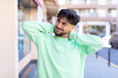 Genç yakışıklı adam endişeli, hasta, hasta ve mutsuz hissediyor, acı verici bir boyun ağrısı çekiyor.