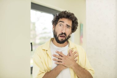 Genç çılgın sakallı adam üzgün, yaralı ve kalbi kırık görünüyor, iki elini de kalbine yakın tutuyor, ağlıyor ve depresif hissediyor.
