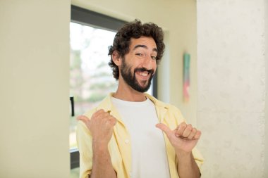 Genç, çılgın, sakallı, neşeli ve tesadüfen gülümseyen bir adam yan taraftaki fotokopi alanını işaret ediyor, mutlu ve tatmin olmuş hissediyor.