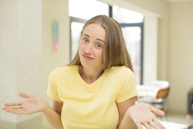 pretty blond woman feeling clueless and confused, having no idea, absolutely puzzled with a dumb or foolish look