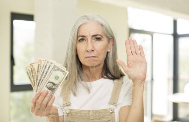 Güzel, son sınıf öğrencisi, ciddi görünüyor. Avuç içi açık, dur hareketi yapıyor. Dolar banknotlarıyla