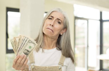 Güzel, yaşlı bir kadın üzgün ve mızmızlanıyor. Mutsuz bir bakışı var ve ağlıyor. Dolar banknotlarıyla