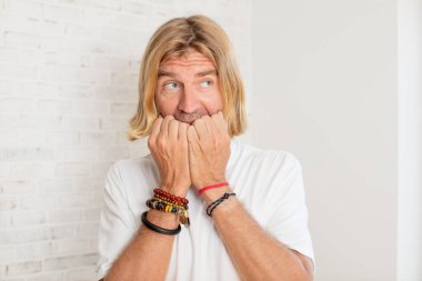 Genç sarışın yetişkin adam endişeli, gergin, stresli ve korkmuş görünüyor, tırnaklarını yiyor ve yanal fotokopi alanı arıyor.