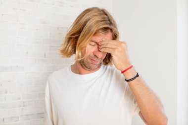 Genç, sarışın, yetişkin bir adam stresli, mutsuz ve hayal kırıklığına uğramış, alınlı ve şiddetli baş ağrısı çeken.