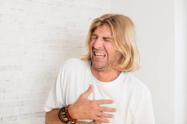 Genç sarışın yetişkin bir adam komik bir şakaya yüksek sesle gülüyor, mutlu ve neşeli hissediyor, eğleniyor.