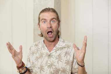 Genç, sarışın yetişkin bir adam mutlu, heyecanlı, şaşırmış ya da şok olmuş, gülümseyen ve hayrete düşmüş hissediyor.