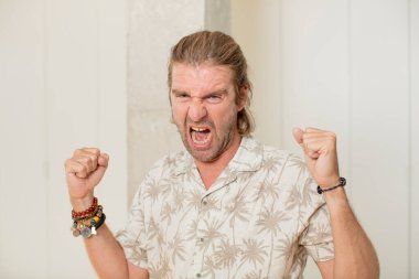 Genç sarışın yetişkin bir adam kızgın bir ifadeyle agresif bir şekilde bağırıyor ya da yumruklarıyla başarıyı kutluyor.