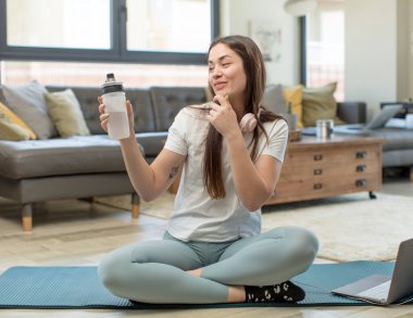 Genç ve güzel bir kadın, mutlu ve kendinden emin bir ifadeyle gülümsüyor, elleri çenesinde. yoga konsepti