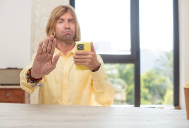 Genç, beyaz bir adam ciddi görünüyor. Avuç içini gösteriyor. Durdurma hareketi yapıyor. akıllı telefon kavramı