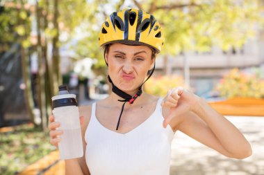 Genç ve güzel bir kadın kendini kötü hissediyor, baş parmağını kaldırıyor. bisiklet kaskı konsepti