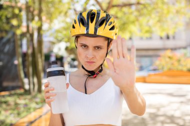 Genç ve güzel bir kadın ciddi görünüyor. Avuç içini gösteriyor. Durdurma hareketi yapıyor. bisiklet kaskı konsepti