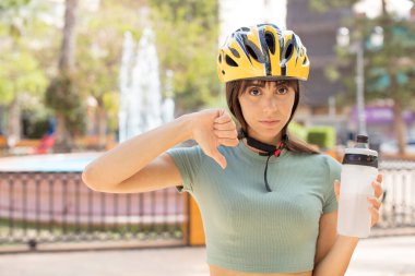Genç ve güzel bir kadın kendini kötü hissediyor, baş parmağını kaldırıyor. bisiklet kaskı konsepti