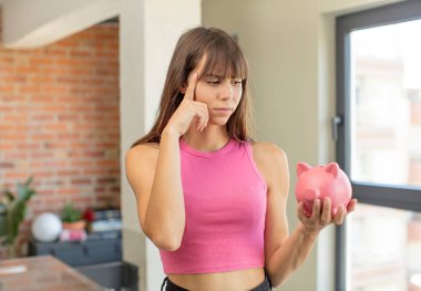 Genç ve güzel bir kadın şaşırmış görünüyor, yeni bir düşünce, fikir ya da konsept domuzcuk banka konseptini fark ediyor.