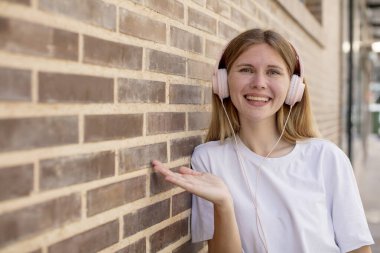 Genç, güzel bir kadın neşeyle gülümsüyor, mutlu hissediyor ve bir konsept gösteriyor. kulaklıklar ve müzik konsepti