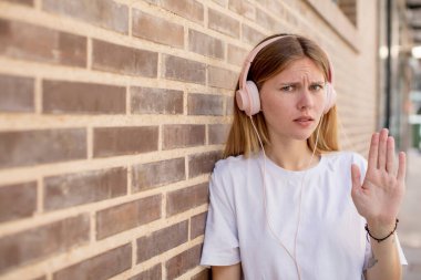 Genç ve güzel bir kadın ciddi görünüyor. Avuç içini gösteriyor. Durdurma hareketi yapıyor. kulaklıklar ve müzik konsepti