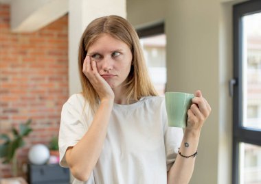 Genç ve güzel bir kadın sıkıcı, bıkkın ve uykulu hissediyor. Kahve fincanı konsepti