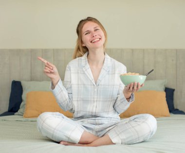 Genç, güzel bir kadın neşeyle gülümsüyor, mutlu hissediyor ve bir tarafı işaret ediyor. Kahvaltı kasesi konsepti