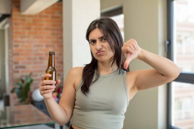 Genç bir kadın kendini kötü hissediyor, baş parmağını kaldırıyor. bira şişesi