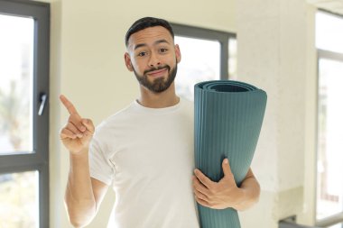 Arap yakışıklı Arap adam, neşeyle gülümseyen, mutlu hisseden ve bir tarafı işaret eden. yoga mat konsepti