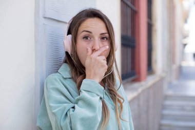 Güzel bir kadın ağzını eliyle kapatıyor ve şok olmuş ya da şaşırmış bir ifade takınıyor. kulaklıklar ve müzik konsepti