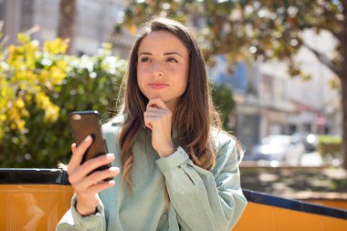 Güzel bir kadın mutlu, kendinden emin ve elleri çenesinde gülümsüyor. akıllı telefon kavramı