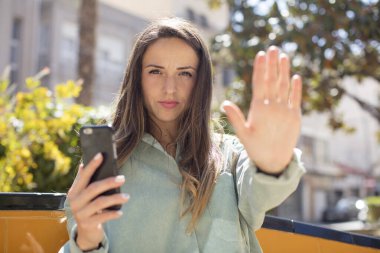 Güzel bir kadın ciddi görünüyor. Avuç içi gösteriyor. Durma hareketi yapıyor. akıllı telefon kavramı