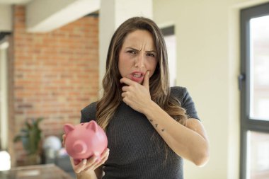 Ağzı ve gözleri açık, eli çenesinde güzel bir kadın. Domuz kumbarası