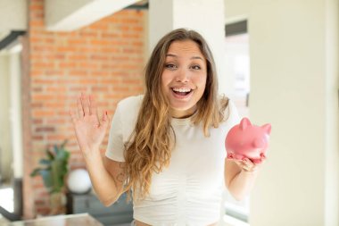 Güzel bir kadın kendini mutlu hissediyor ve inanılmaz bir şeye hayret ediyor. Domuz kumbarası konsepti