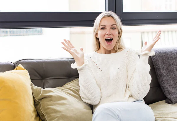 stock image young pretty woman feeling happy, excited, surprised or shocked, smiling and astonished at something unbelievable sitting on a couch