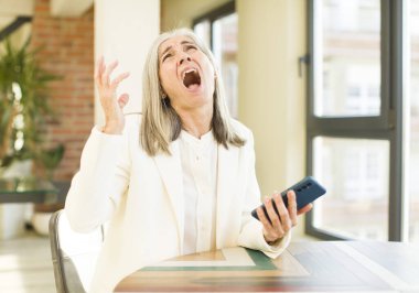 Güzel, son sınıf öğrencisi bir kadın akıllı telefonuyla ellerini havaya kaldırarak bağırıyor.