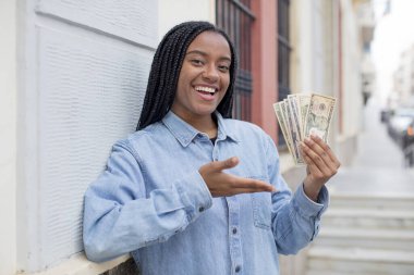 Siyah afro kadın neşeyle gülümsüyor, mutlu hissediyor ve bir konsept gösteriyor. Dolar banknotları konsepti