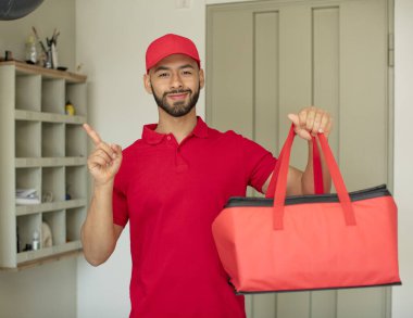 Genç yetişkin bir adam neşeyle gülümsüyor, mutlu hissediyor ve bir tarafı işaret ediyor. Pizza teslimatçısı konsepti