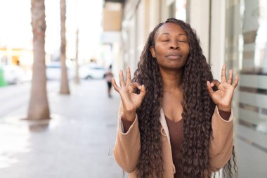 Afro güzel siyah kadın konsantre olmuş ve meditasyon yapıyor, tatmin olmuş ve rahatlamış hissediyor, düşünüyor ya da bir seçim yapıyor.