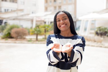 Afro güzel siyah kadın mutlu bir şekilde gülümsüyor, arkadaş canlısı, kendinden emin, pozitif bakışlı, bir nesne ya da konsept sunuyor ve gösteriyor.