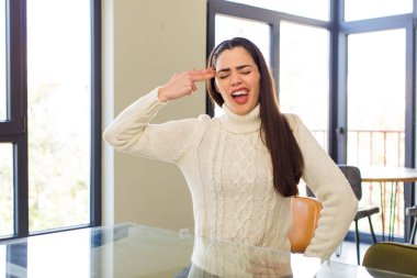 pretty caucasian woman looking unhappy and stressed, suicide gesture making gun sign with hand, pointing to head