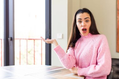 pretty caucasian woman looking surprised and shocked, with jaw dropped holding an object with an open hand on the side