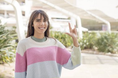 Güzel genç bir kadın kendini mutlu, eğlenceli, kendinden emin, pozitif ve asi hissediyor, elle rock ya da heavy metal işareti yapıyor.