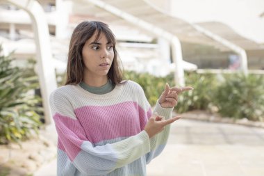 Güzel, genç bir kadın şaşkın ve şaşırmış hissediyor. Yan taraftaki fotokopi alanını işaret ediyor. Şaşırmış ve ağzı açık bakıyor.