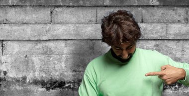 Neşeli bir şekilde gülümsüyor, aşağıya bakıyor ve göğsünü işaret ediyor.