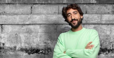 Kameraya çapraz kollarla gülümsüyor ve mutlu, kendinden emin, tatmin olmuş bir ifade, yan görüş.