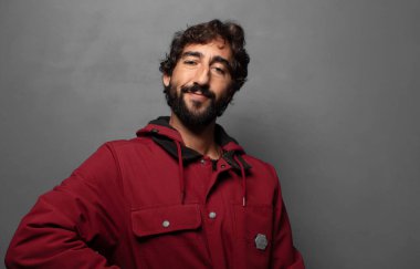 Mutlu bir şekilde gülümsüyor, eli kalçasında ve kendinden emin, olumlu, gururlu ve arkadaş canlısı bir tavırla.